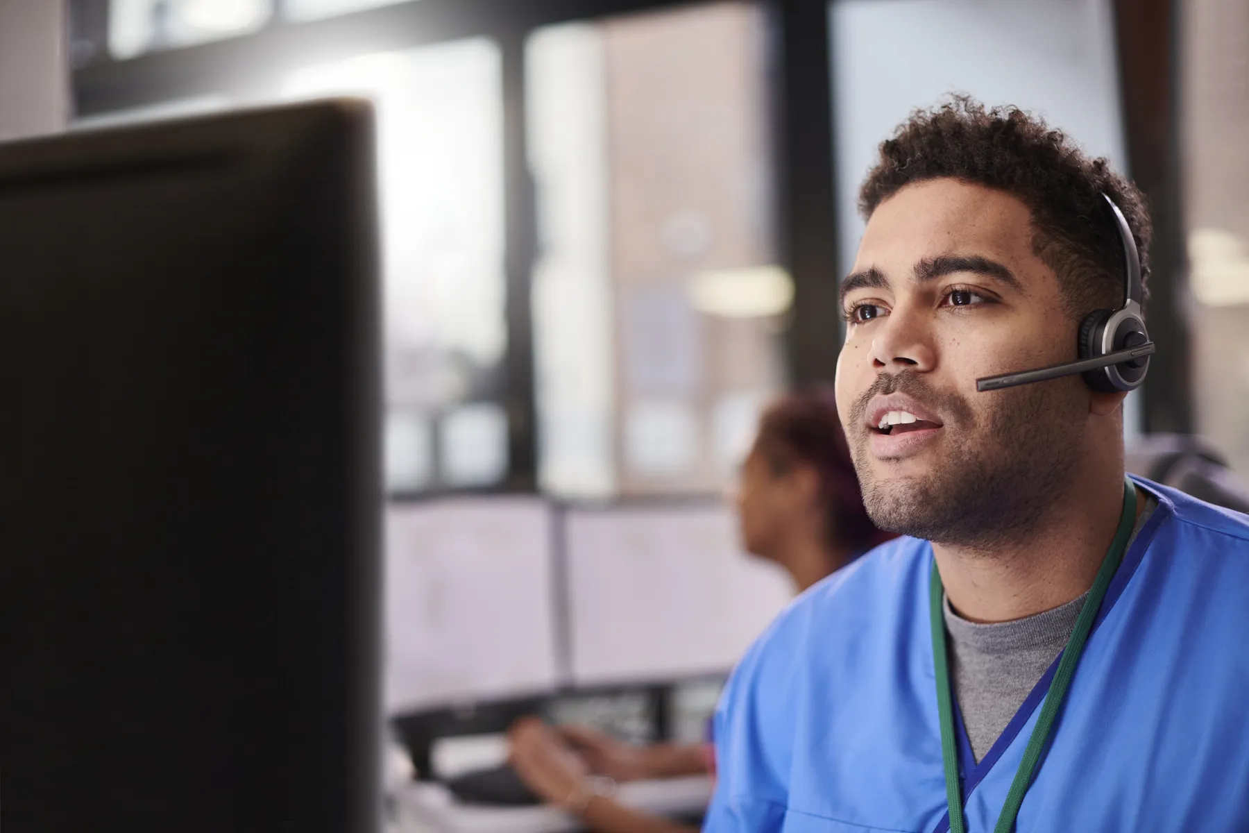 A contact center agent in scrubs speaking into his headset at a workstation