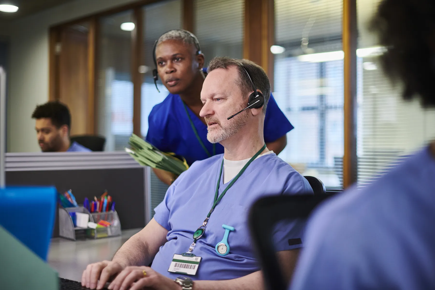 Healthcare contact center agents in scrubs, one wearing a headset at his desk