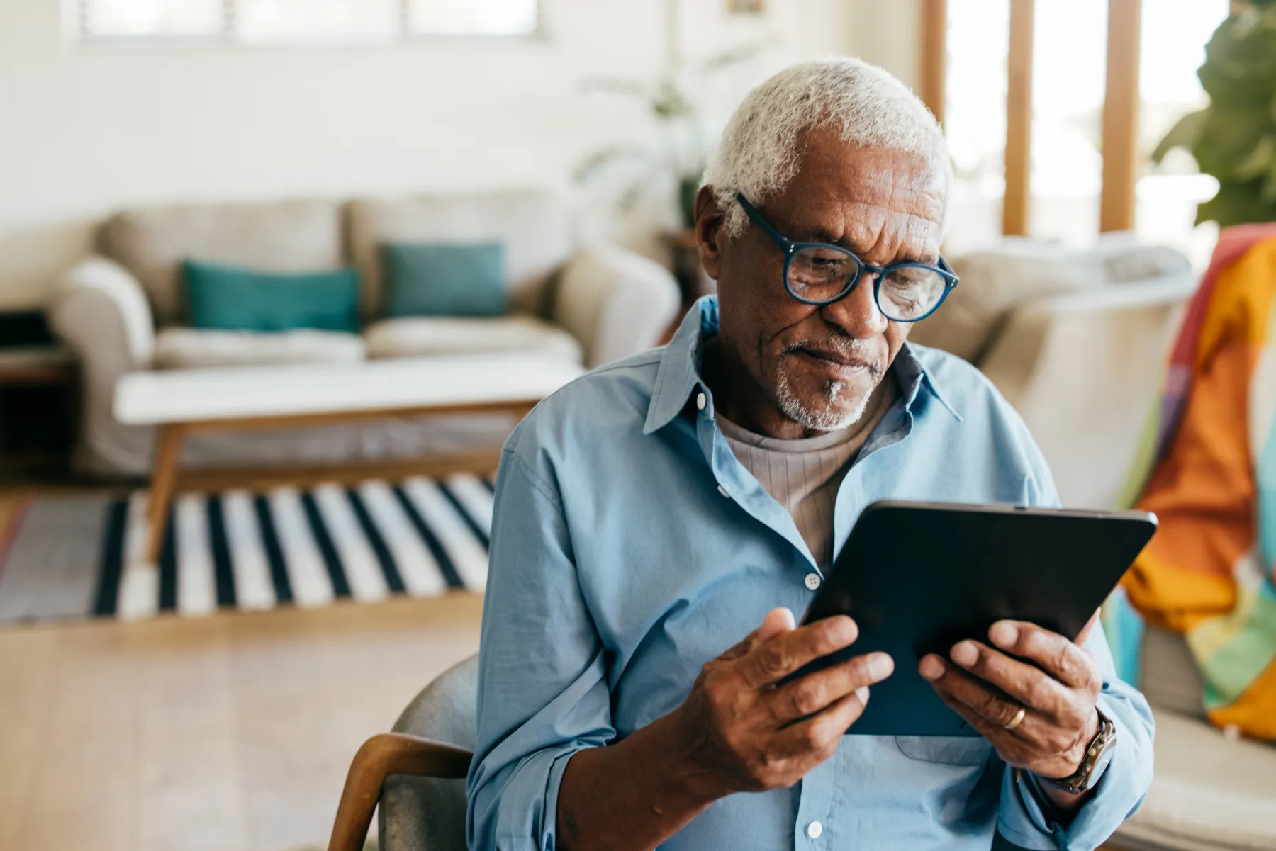 An older man in glasses reading a tablet at home