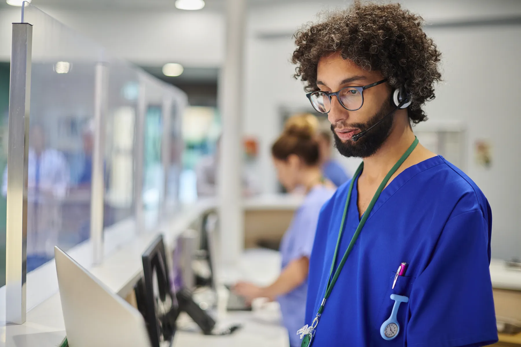 A patient access agent in scrubs and a headset at a front desk workstation
