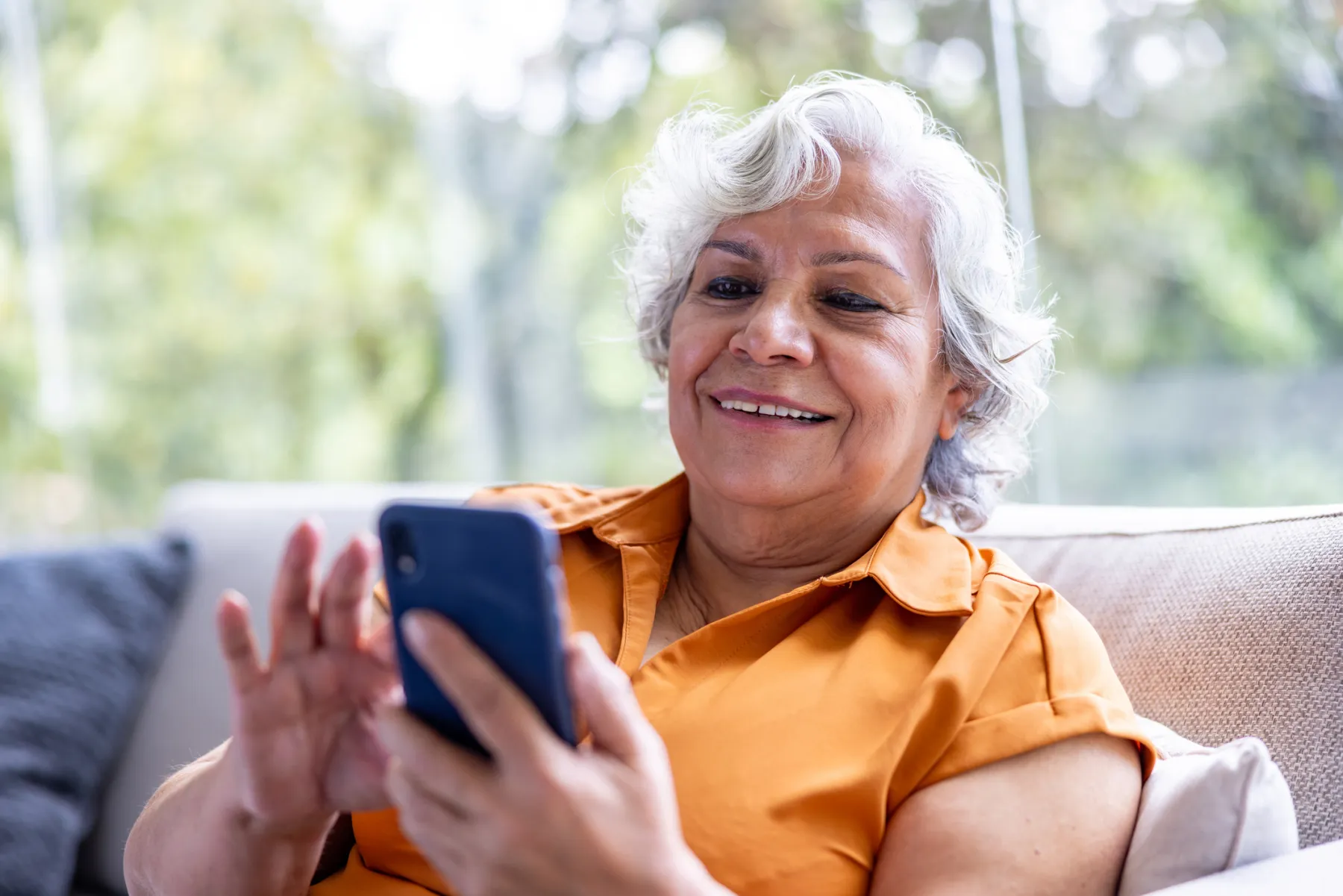 A smiling older woman on a sofa, reading her smartphone