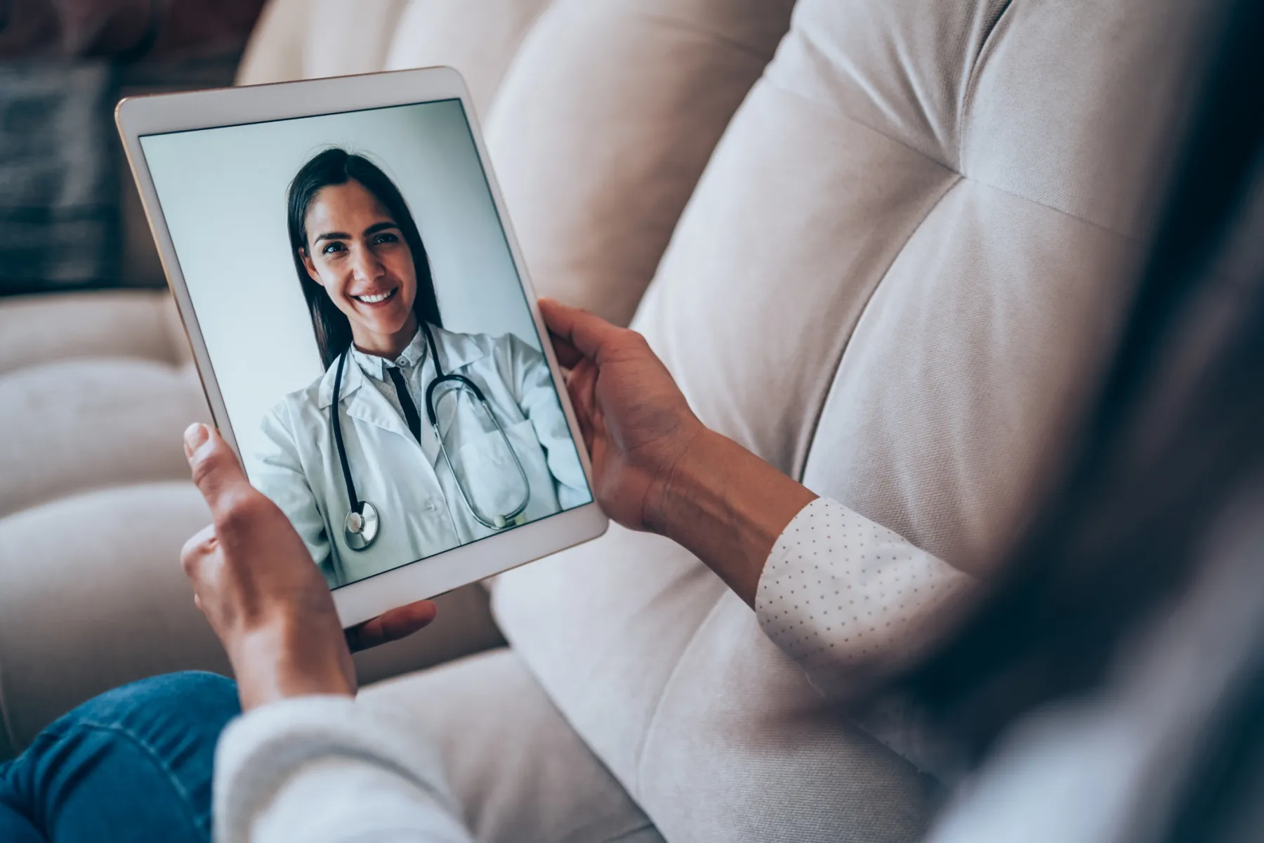 A patient holding a tablet during a video visit with a smiling doctor