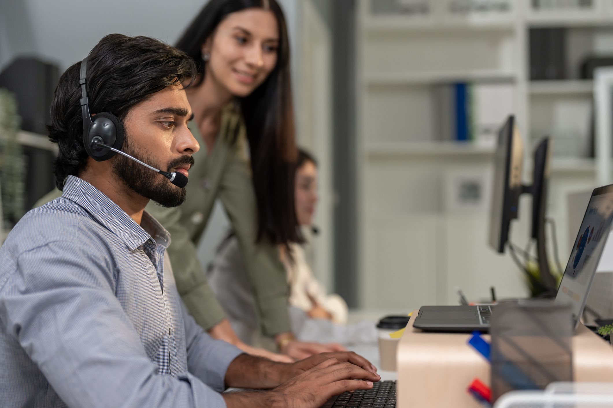 Supervisor standing beside a seated agent on a headset call